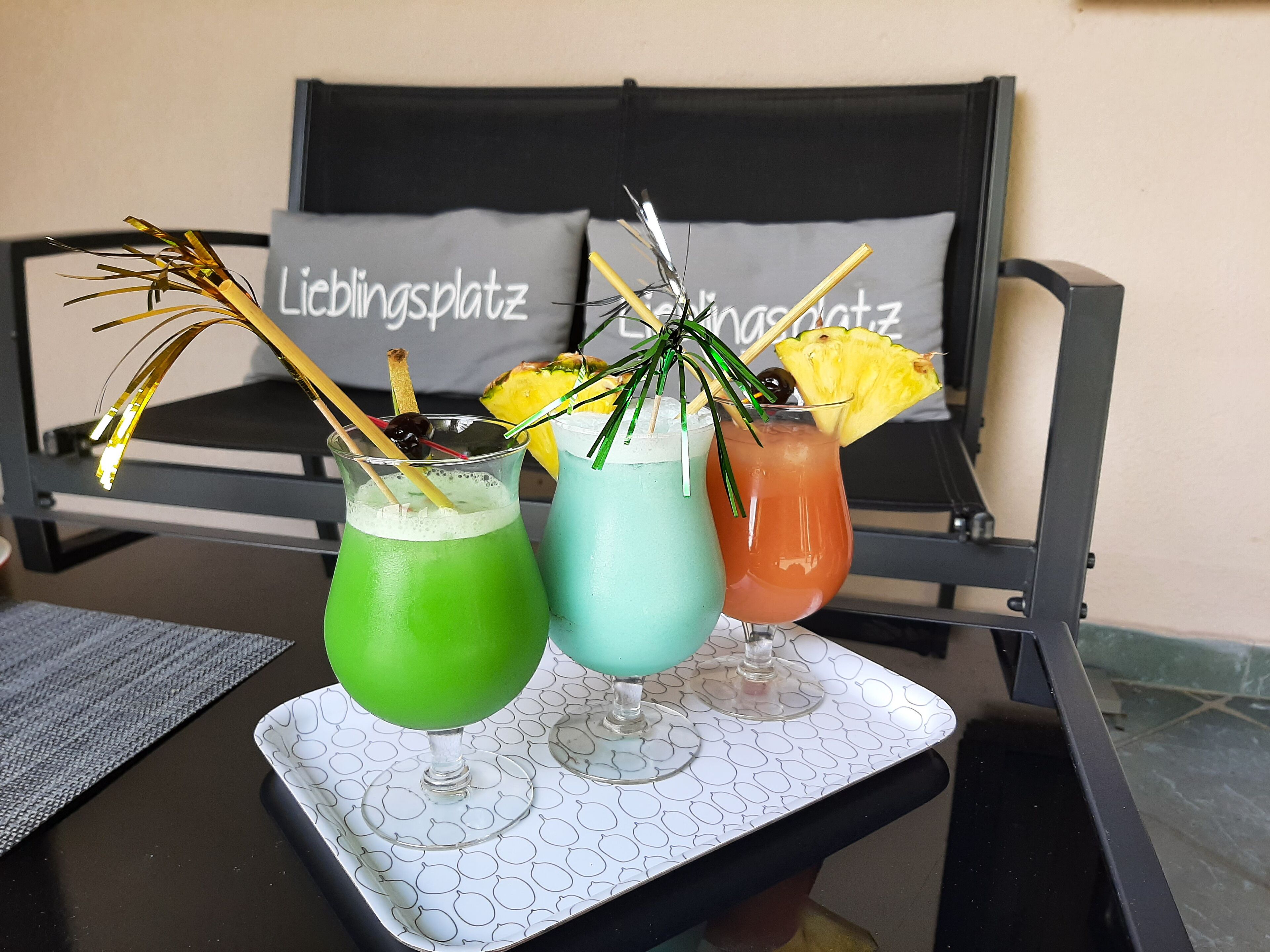 A table with three drinks, a tray, and a couch with pillows in the background.