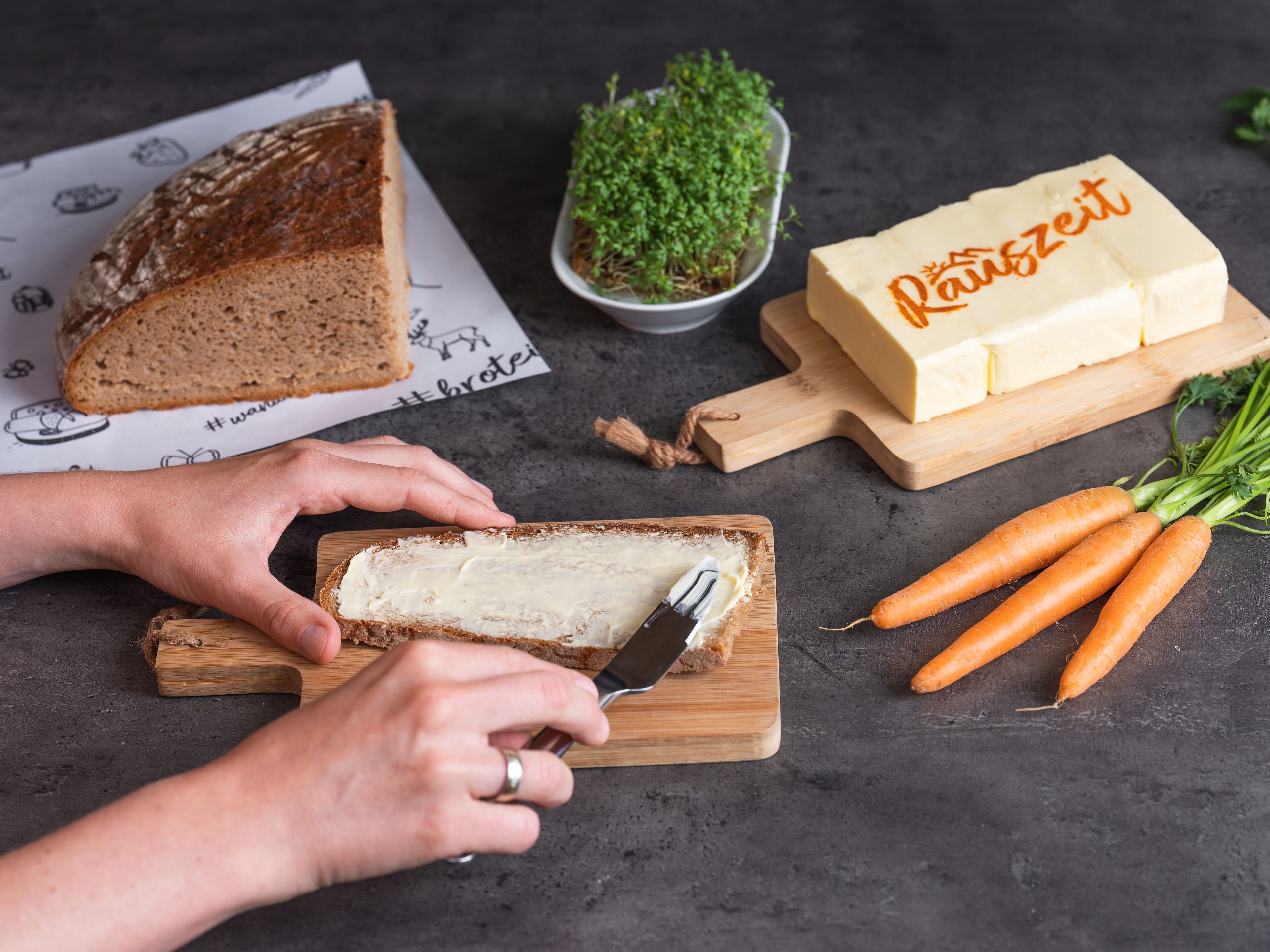 Une personne tartine du beurre sur une tranche de pain, sur une planche à découper en bois.
