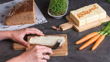 Une personne tartine du beurre sur une tranche de pain, sur une planche à découper en bois.