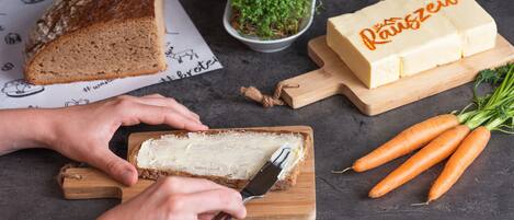 A person spreading butter on a slice of bread on a wooden cutting board.