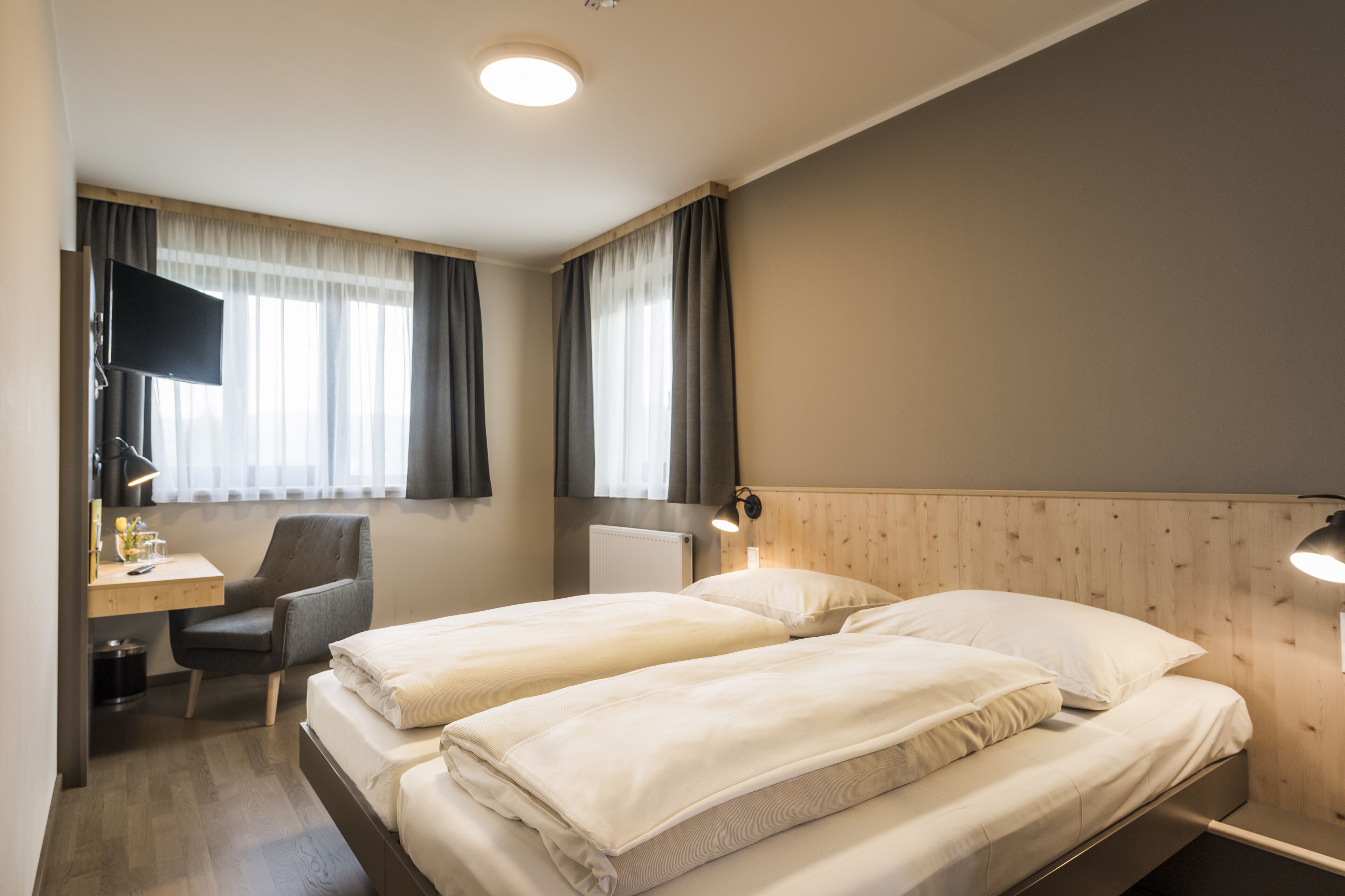 A hotel room with two beds, a desk with a chair, a TV, and a lamp.