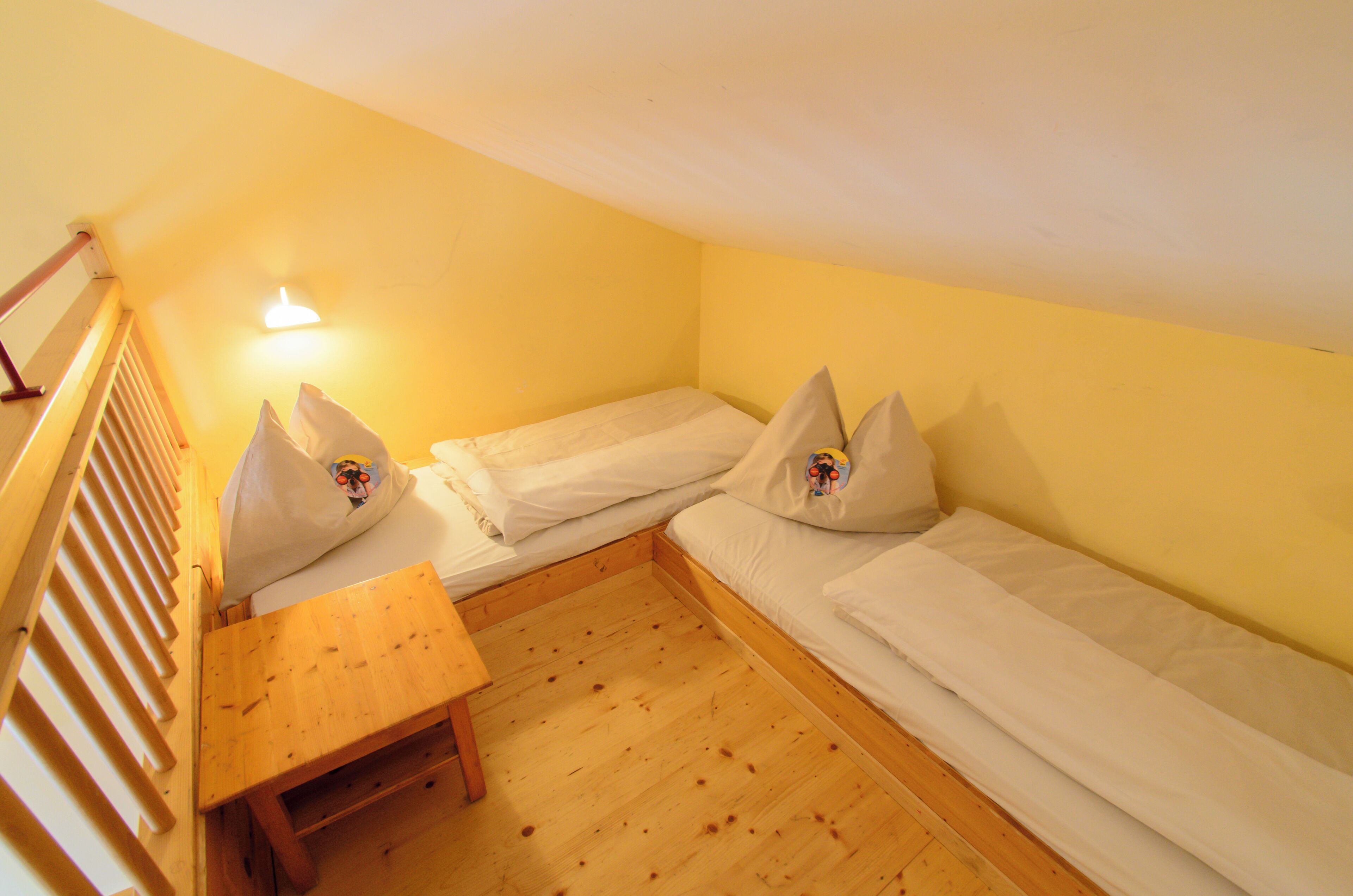 Una habitación pequeña y acogedora con dos camas individuales, una mesa de madera y un banco.