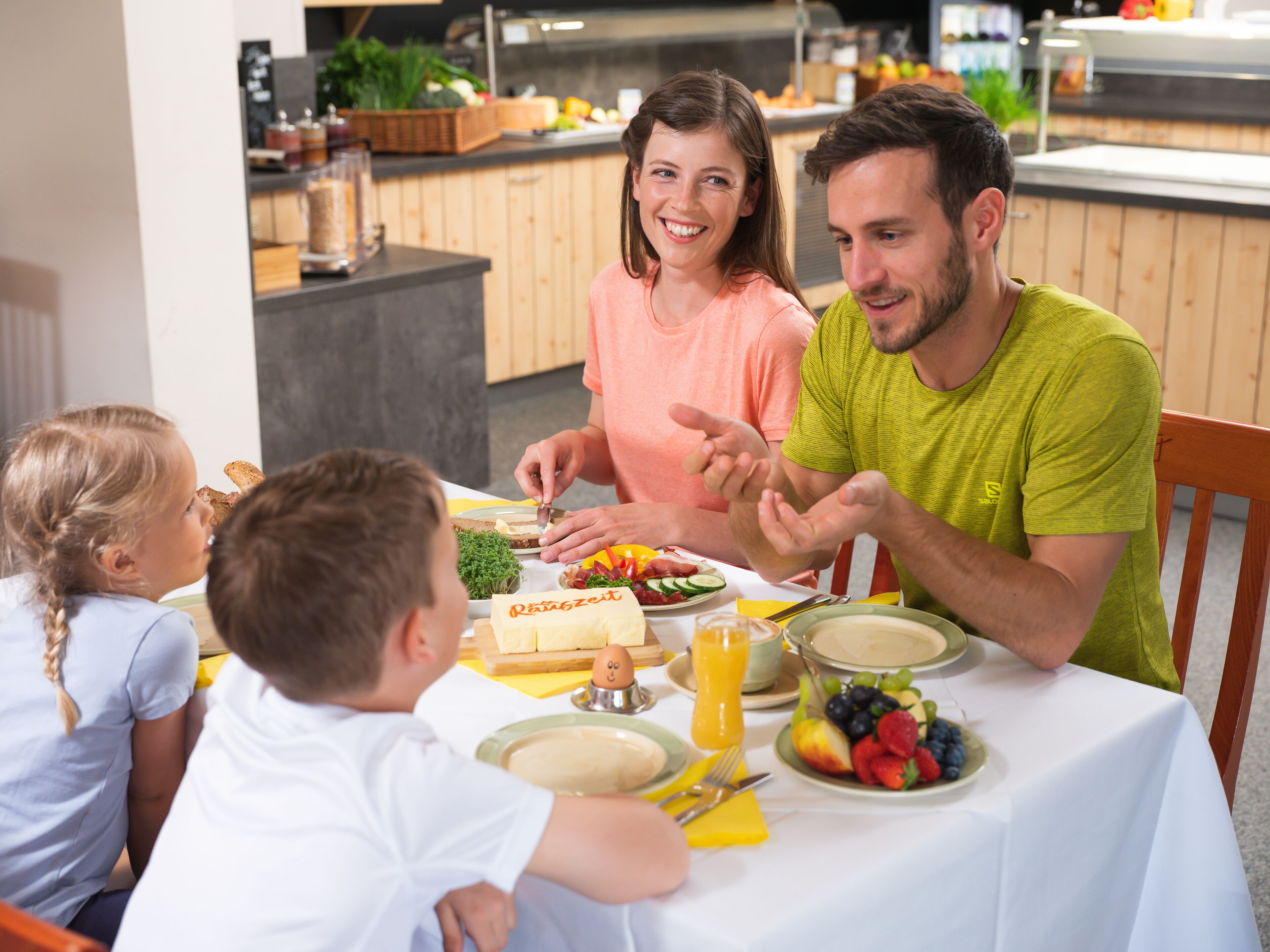 A family dining at a table with breakfast items, including bread, fruit, and juice.
