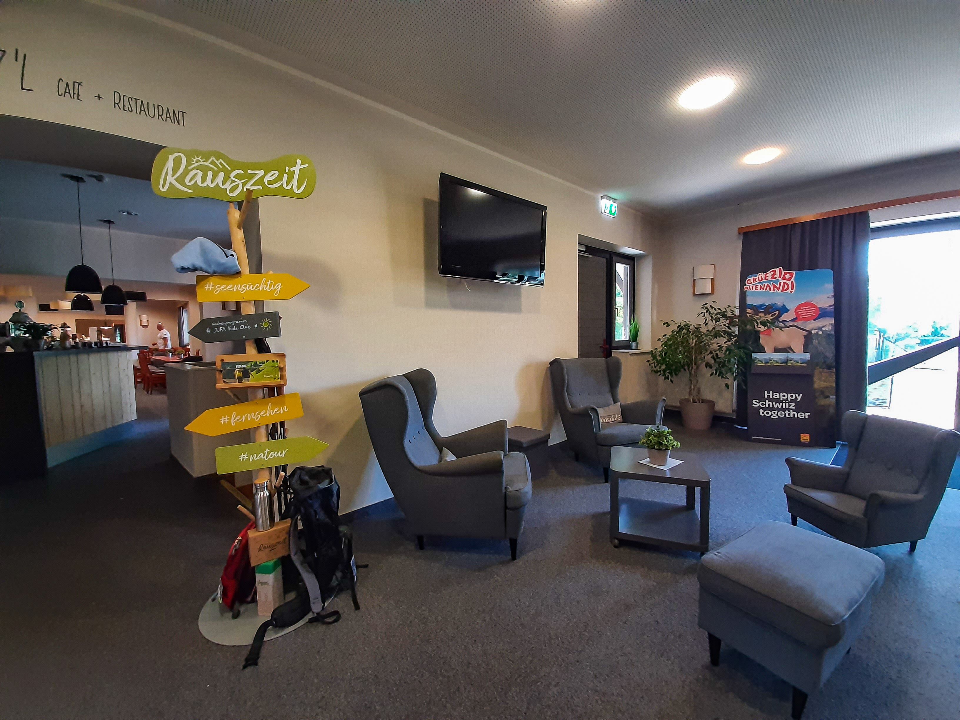Vestíbulo de hotel con asientos, una recepción, un televisor y señales de dirección.