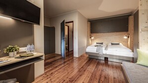 A modern bedroom with a bed, bedside tables, a TV, and a wooden ceiling. - JUFA Hotel Maria Lankowitz am See (Maria Lankowitz)