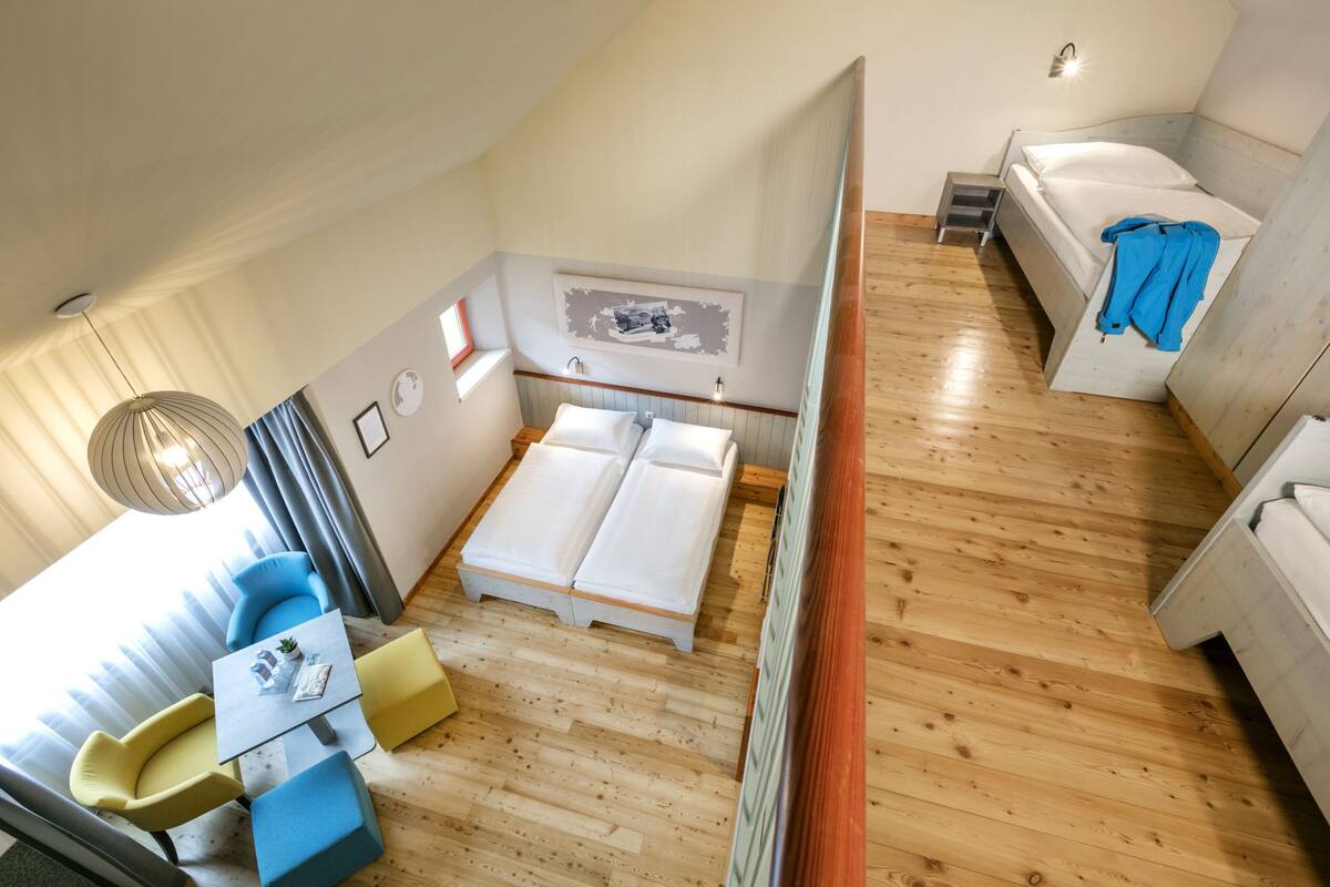 Een kleine kamer met een bed, een tafeltje met stoelen en een raam met gordijnen.