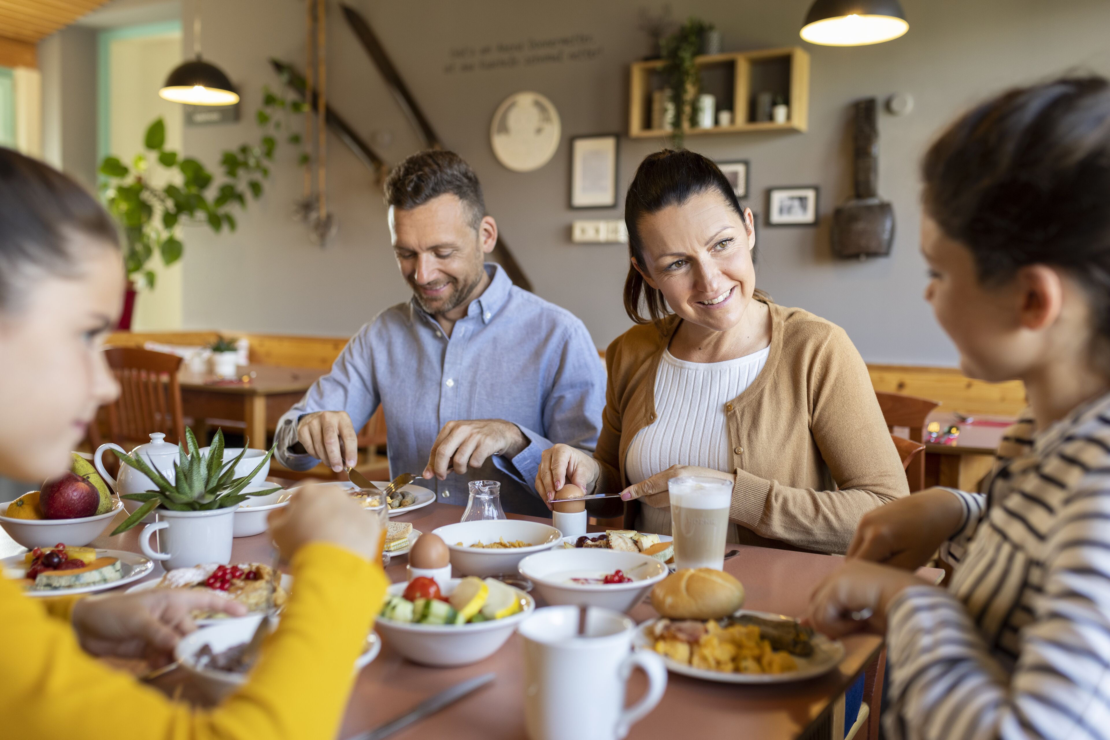 Una familia comiendo en una mesa con varios platos, incluyendo frutas, pan y una taza blanca.
