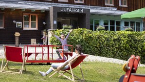 A wooden building with a sign reading "JUFA Hotel" and a playground with red equipment.