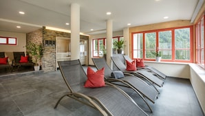 A spacious indoor area with reclining chairs, a stone wall, and large windows with red frames.