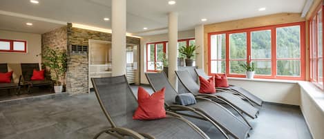 A spacious indoor area with reclining chairs, a stone wall, and large windows with red frames.