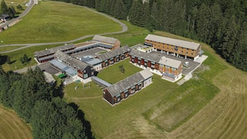 An aerial view of a modern building complex with multiple structures, surrounded by green fields and dense forest.