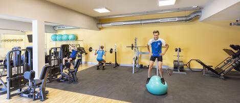 A gym with exercise equipment, a mirrored wall, and a yellow wall.