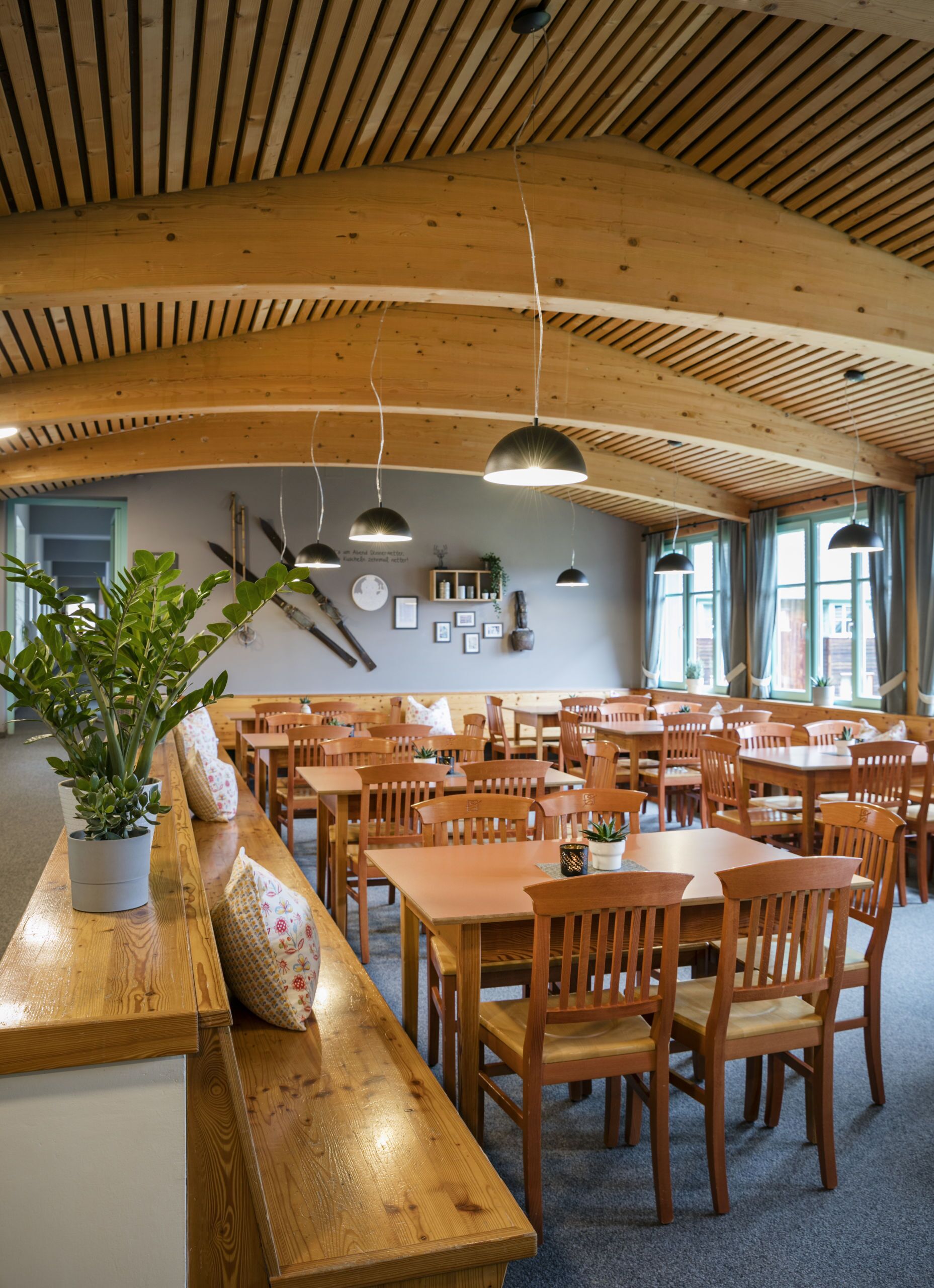 A spacious dining area with wooden tables and chairs, a long bench, and hanging pendant lights.