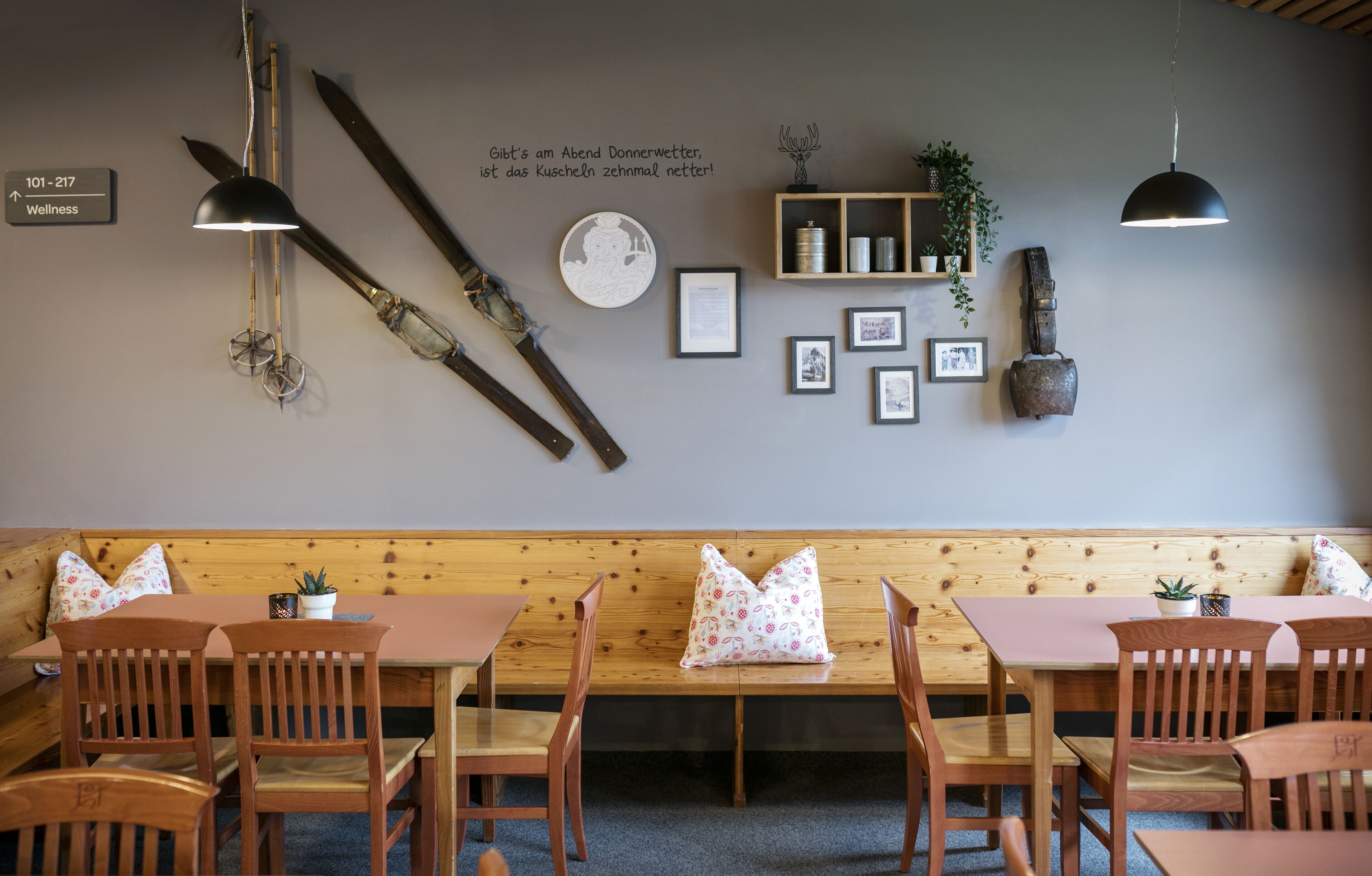 Un interior de restaurante con mesas y bancos de madera, esquíes en la pared y un cartel que indica servicios de bienestar.