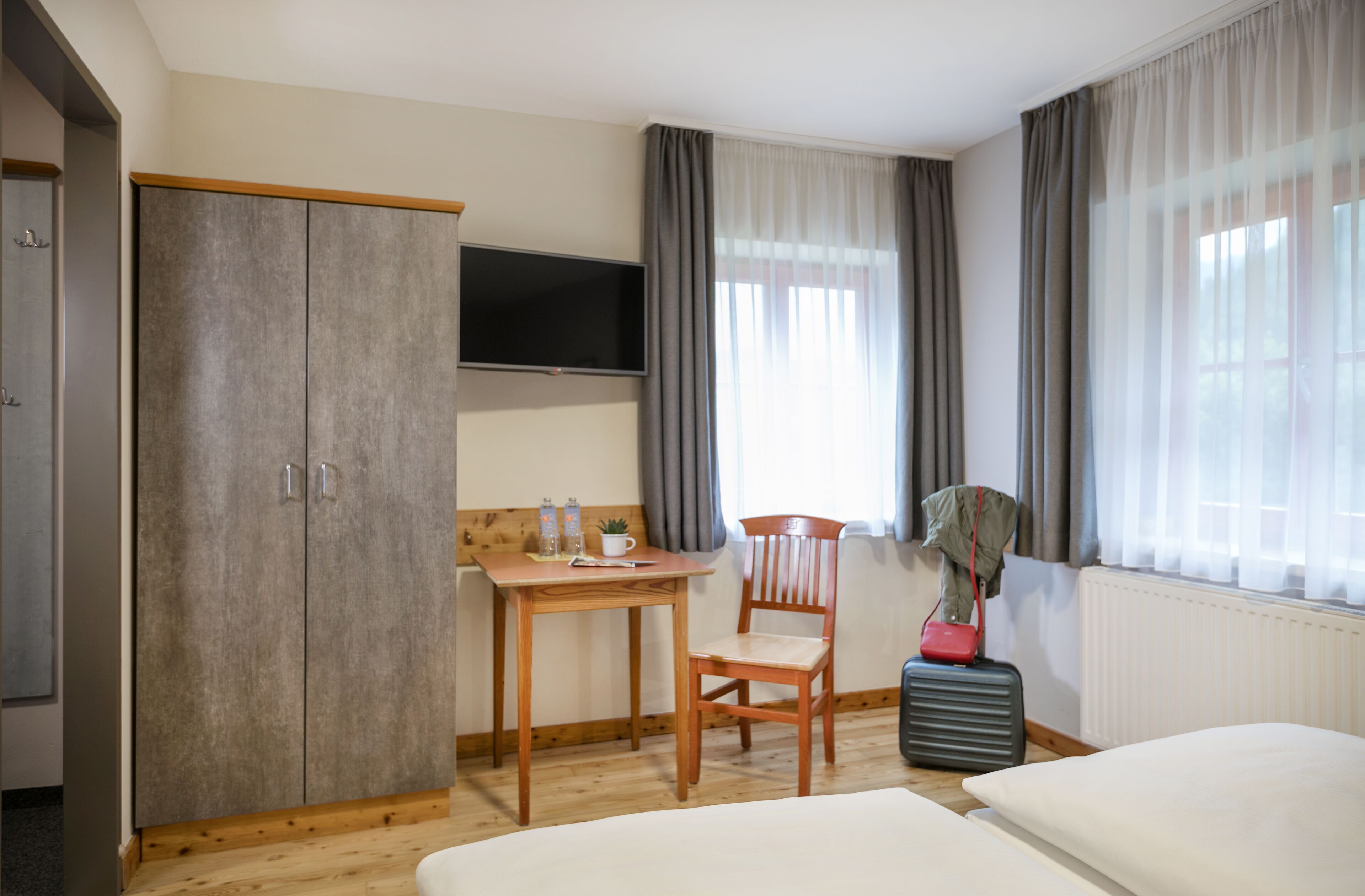 Una habitación de hotel con cama, escritorio con silla, televisor y armario.