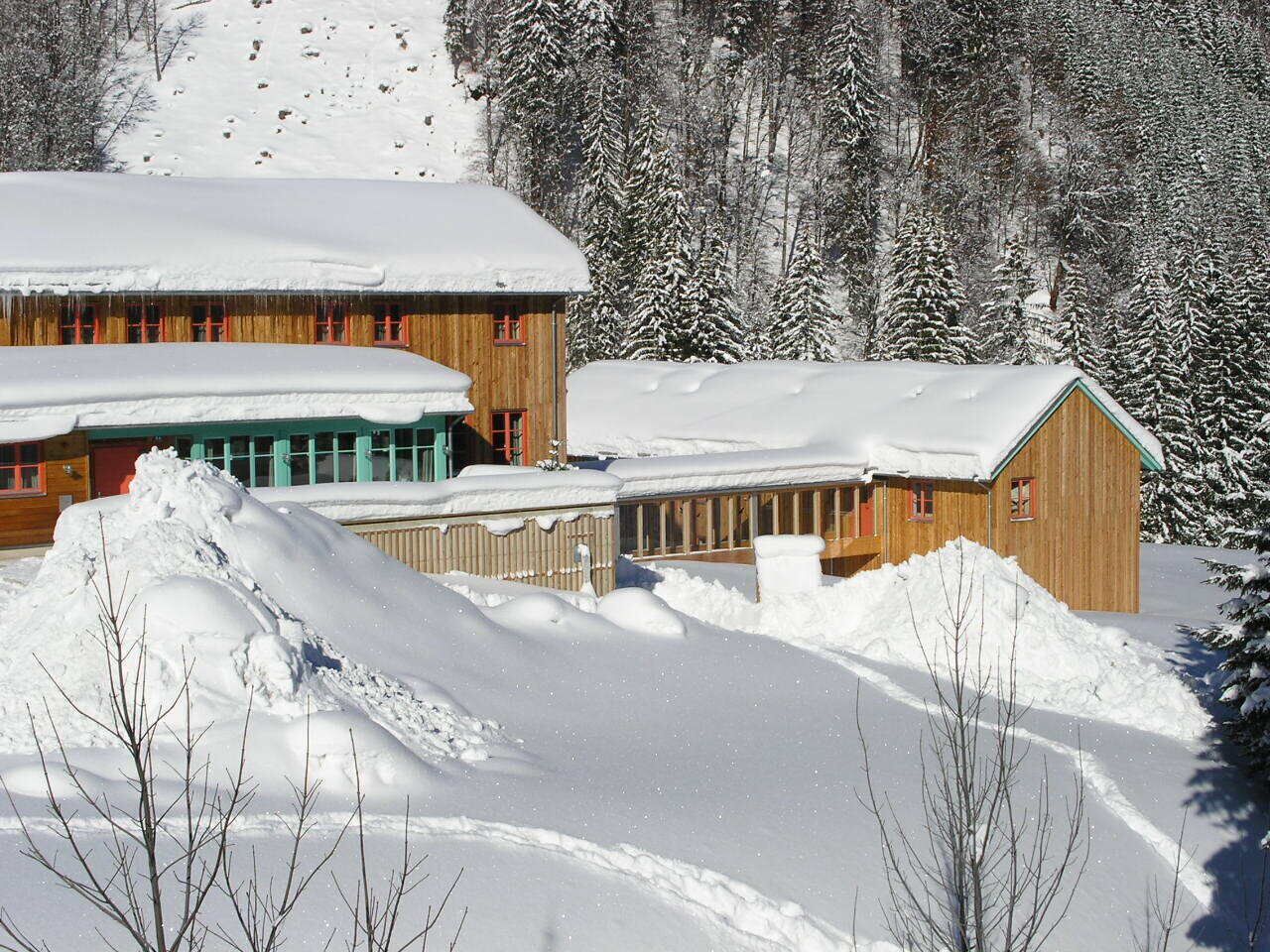 Un chalet en bois, dont le toit est recouvert de neige, et devant lequel se trouve un grand amas de neige.