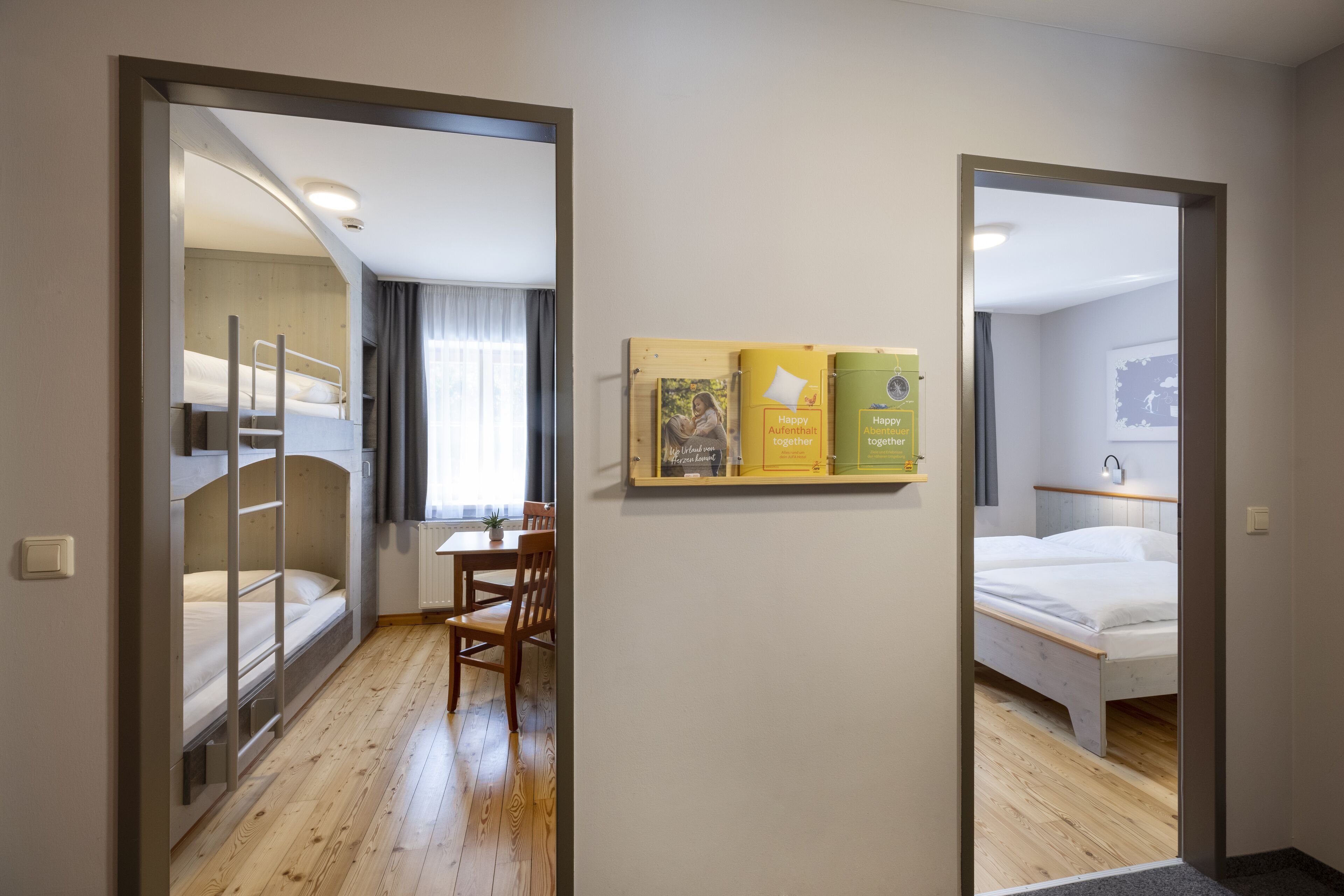 A hotel room with a bunk bed, a desk with a chair, and a bed. There are two framed items on the wall.