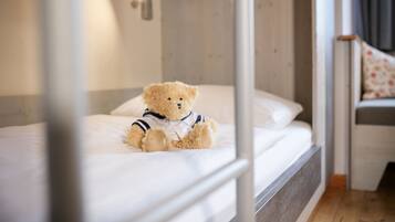 A single bed with a teddy bear on it, a bedside table, and a small chair with a floral cushion.
