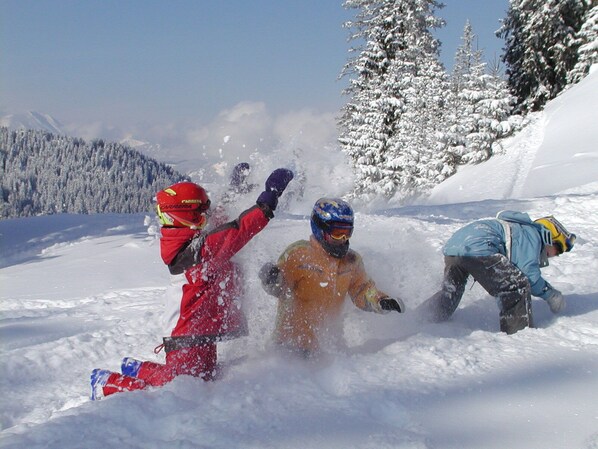 Paisaje nevado con una persona en una chaqueta roja y casco, otra en una chaqueta naranja y una tercera en una chaqueta azul.