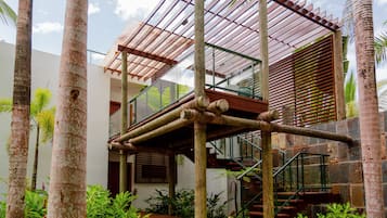 A modern house with a wooden staircase, a glass balcony, and lush greenery.