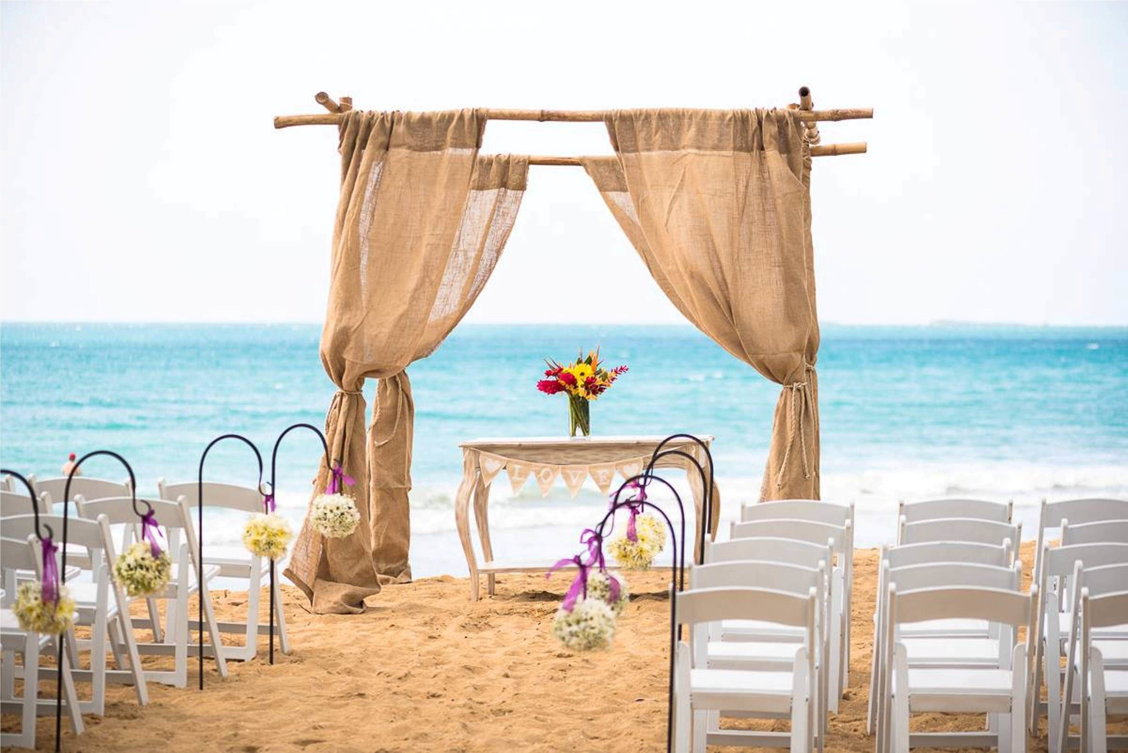 A beach wedding setup with a wooden arch and white chairs.