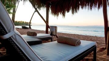 A beachside lounge with two reclining chairs, a small table, and a bottle of water.