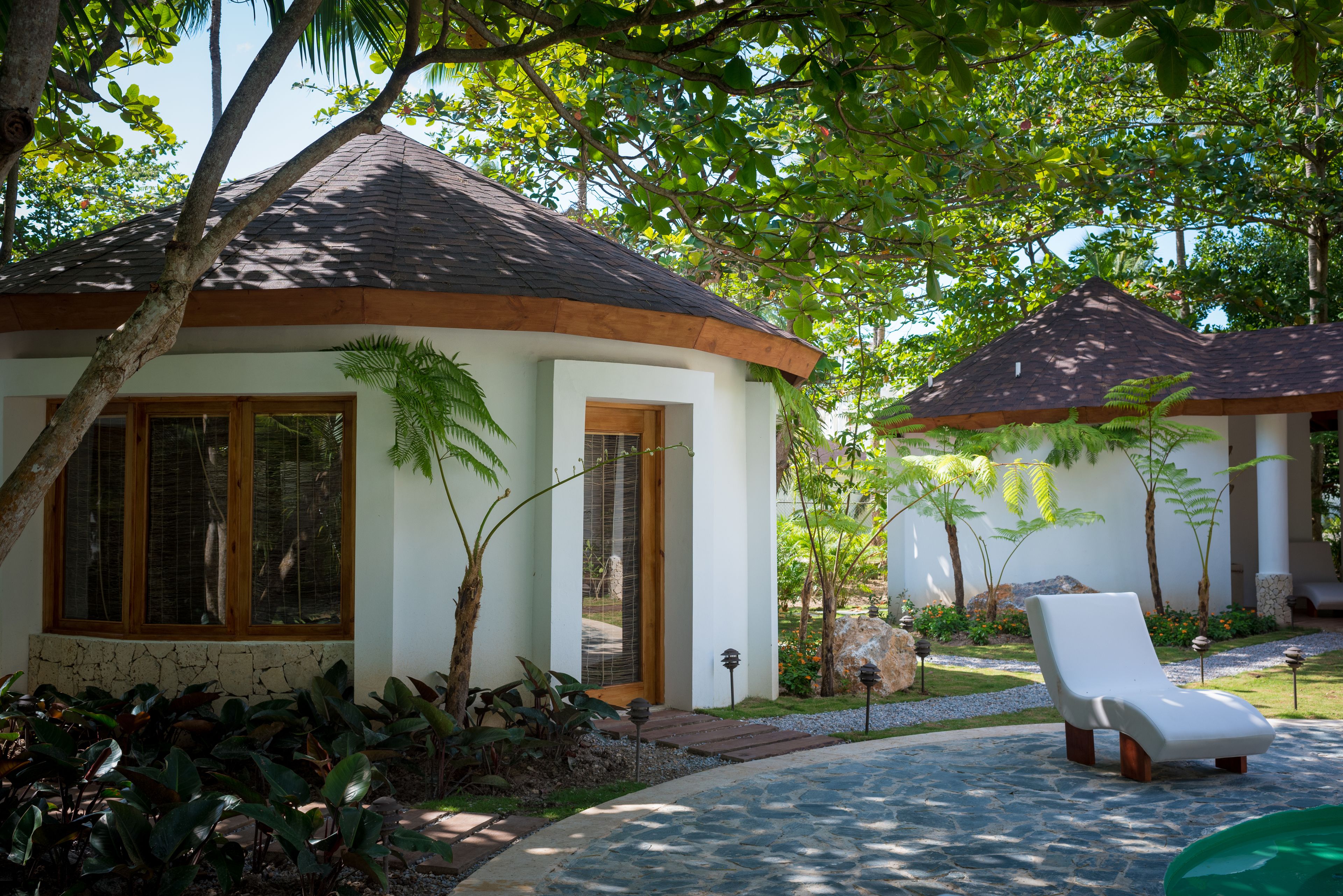 A resort with a covered lounge area, a stone pathway, and lush greenery.