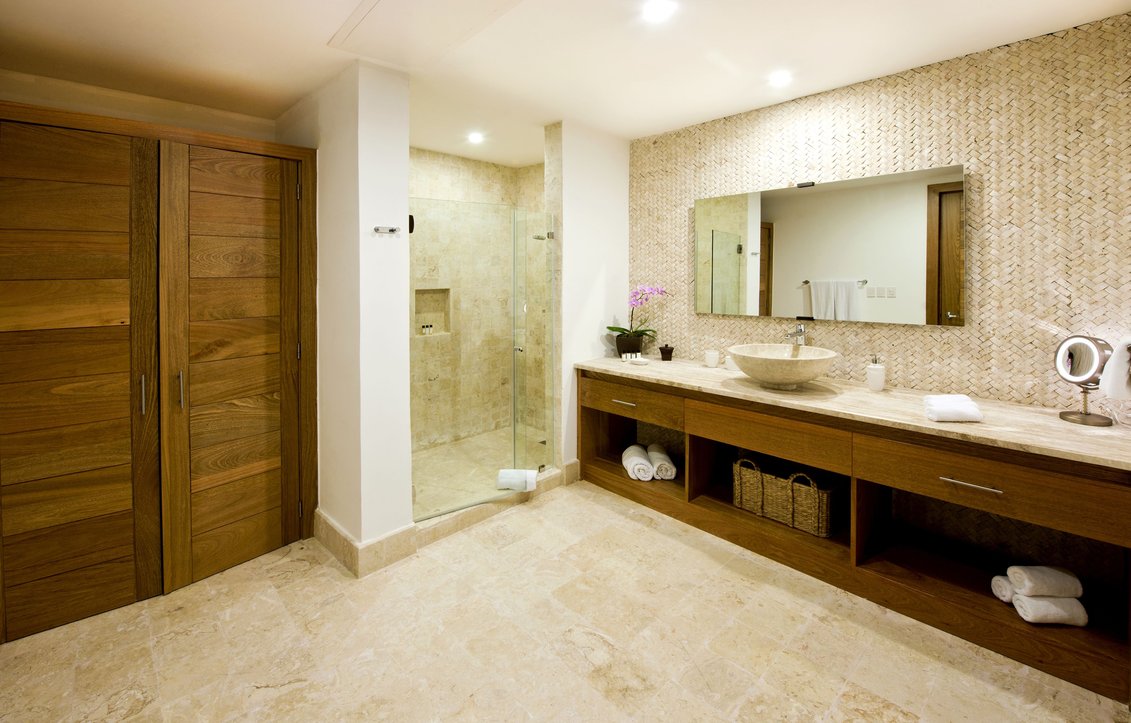 Une salle de bain moderne avec un placard en bois, une cabine de douche en verre, un lavabo avec un miroir et un sol carrelé.