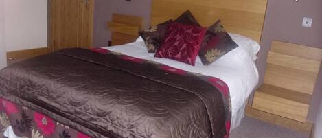 A bed with a wooden headboard, a brown and red patterned bedspread, and several pillows with floral designs.