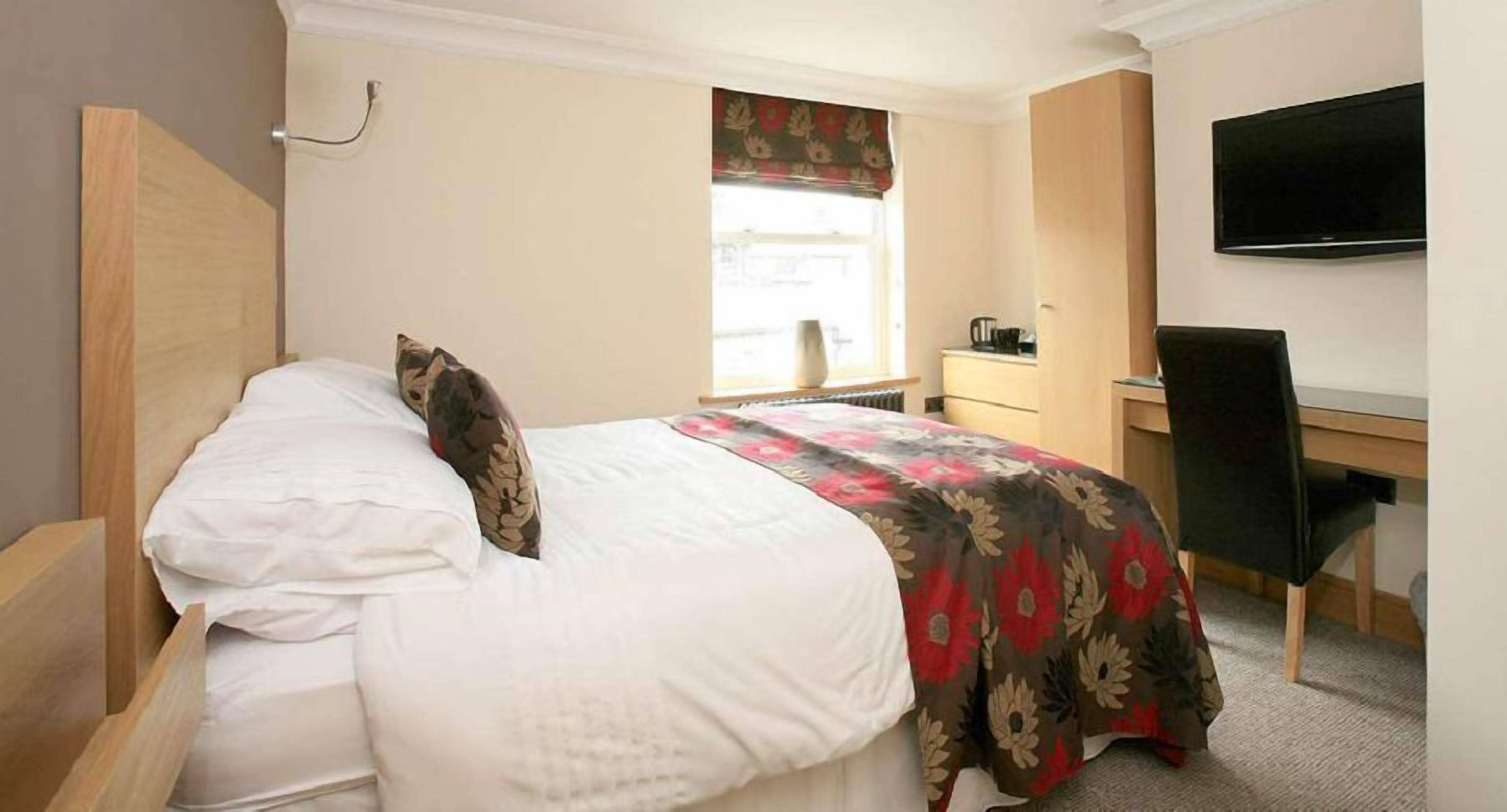 A hotel room with a bed, a desk, a chair, a television, and a window with curtains.