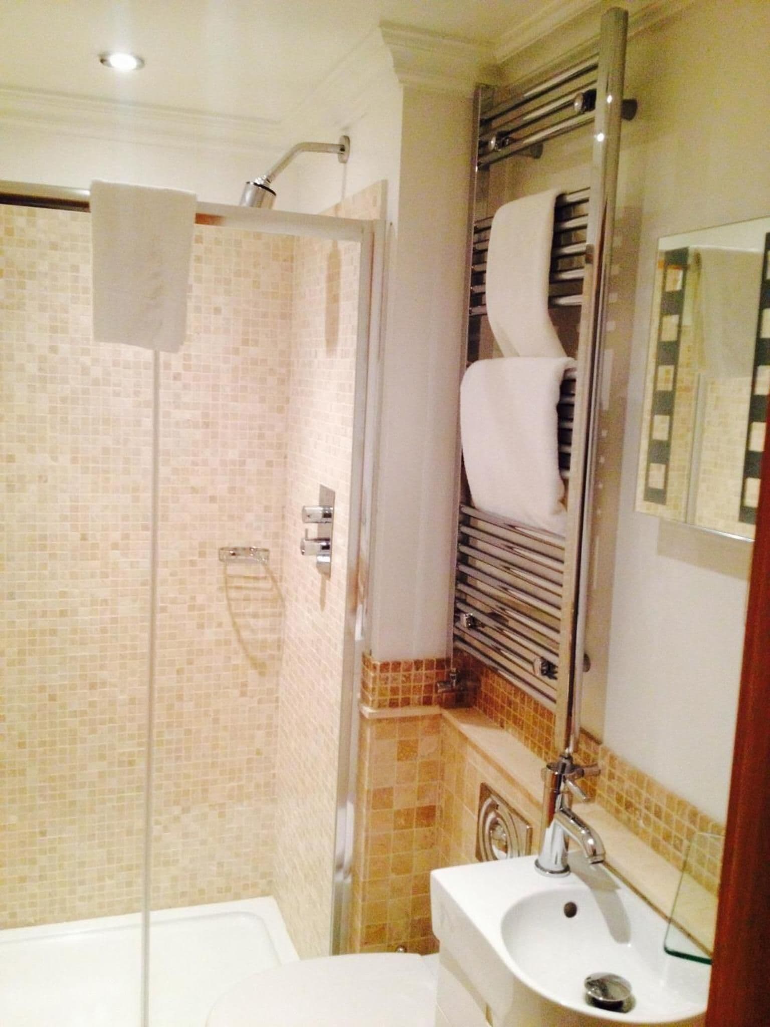 Un baño con ducha envuelta en vidrio, un lavabo blanco y un perchero para toallas.
