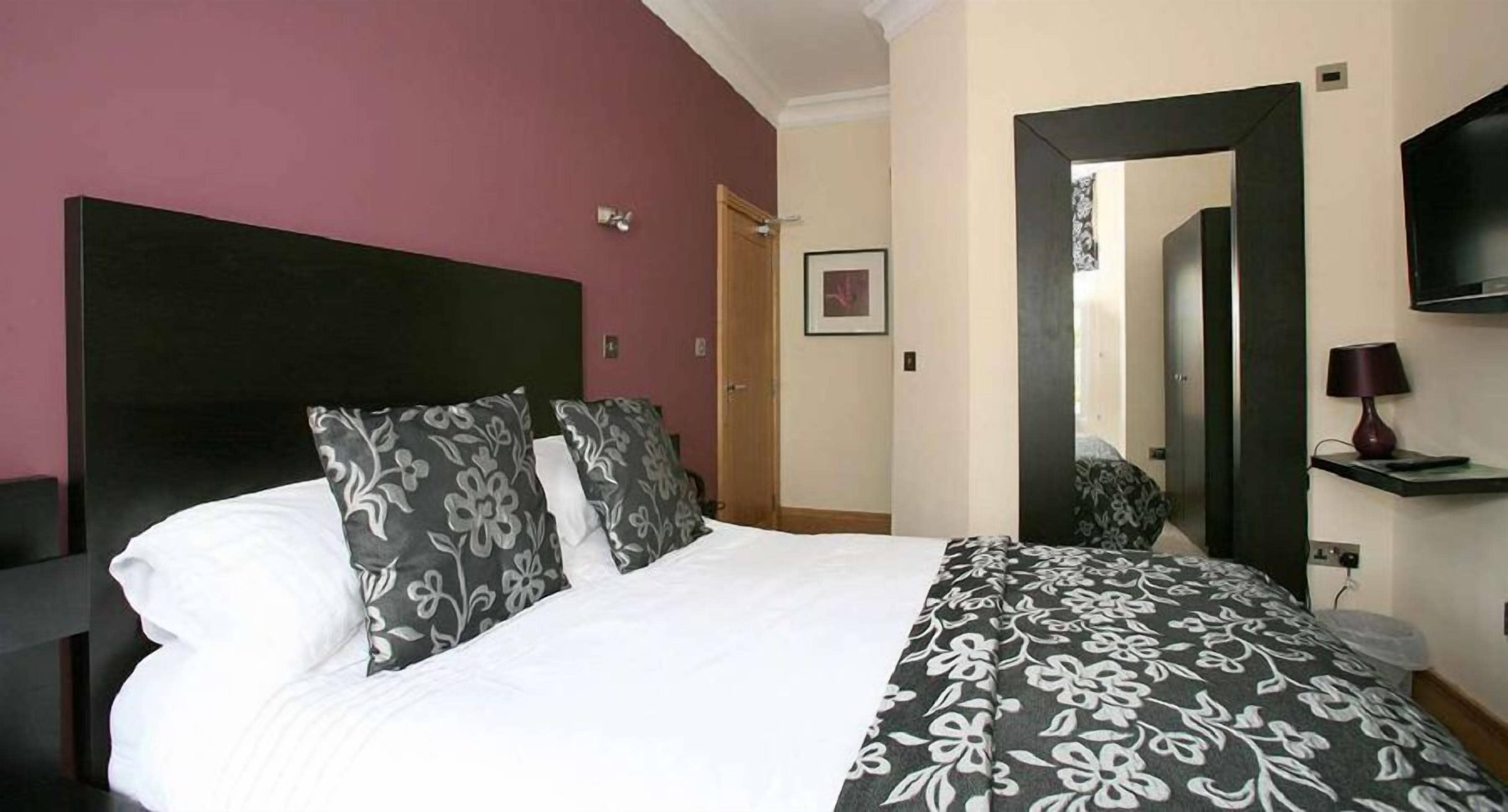 A hotel room with a large bed, a dark headboard, a television, and a mirror.