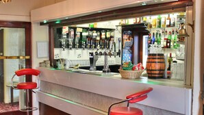 Una zona de bar con dos taburetes rojos, una barra con una variedad de botellas y un barril de madera decorativo.