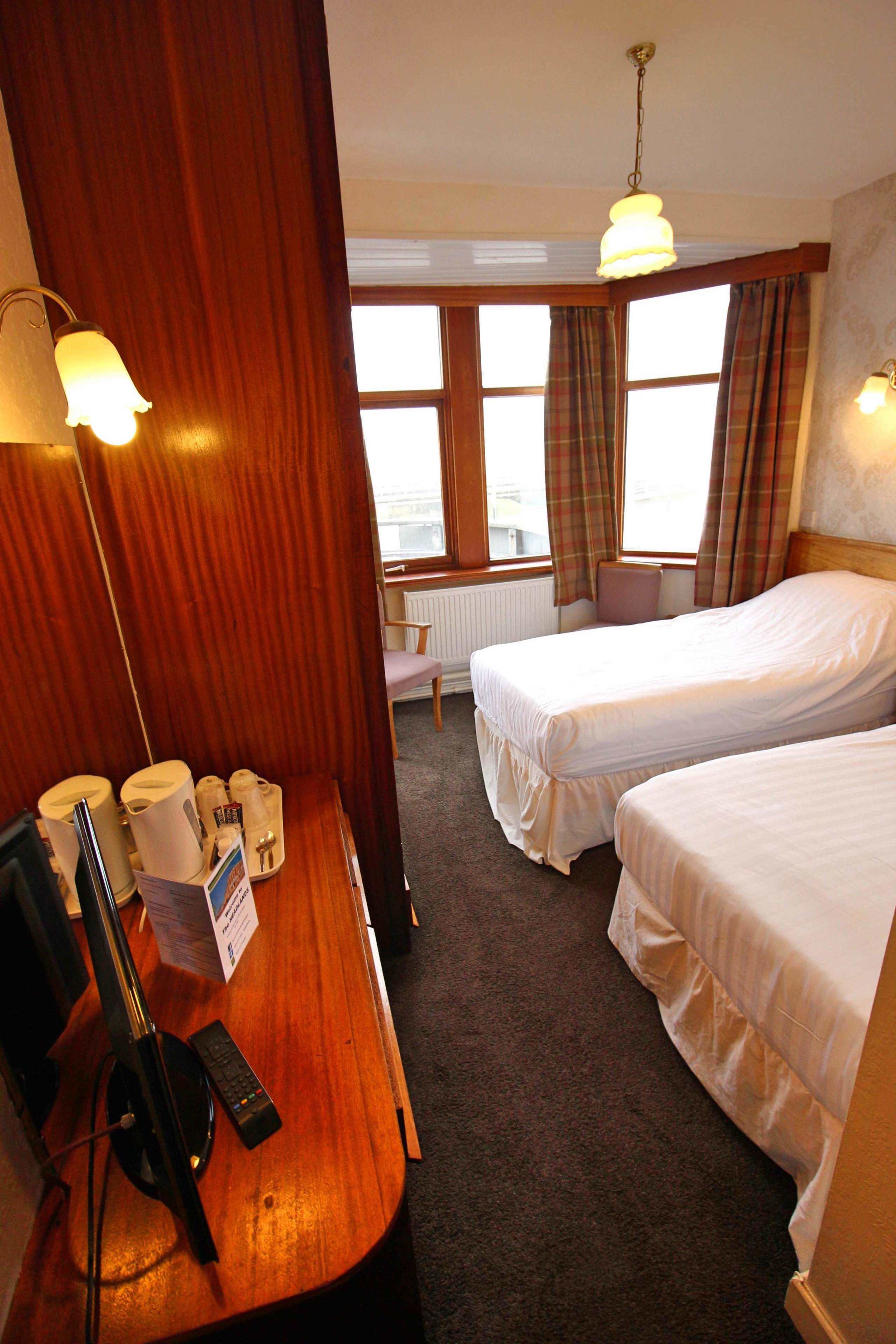 Ein Hotelzimmer mit zwei Einzelbetten, einem Holztisch mit Lampe, einem Stuhl und einem Fenster mit Vorhängen.