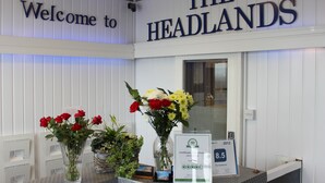 Un mostrador de recepción con un cartel que dice 'Welcome to THE HEADLANDS', un certificado y arreglos florales.