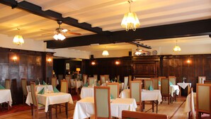 Comedor con varias mesas y sillas, vigas de madera en el techo y candelabros.