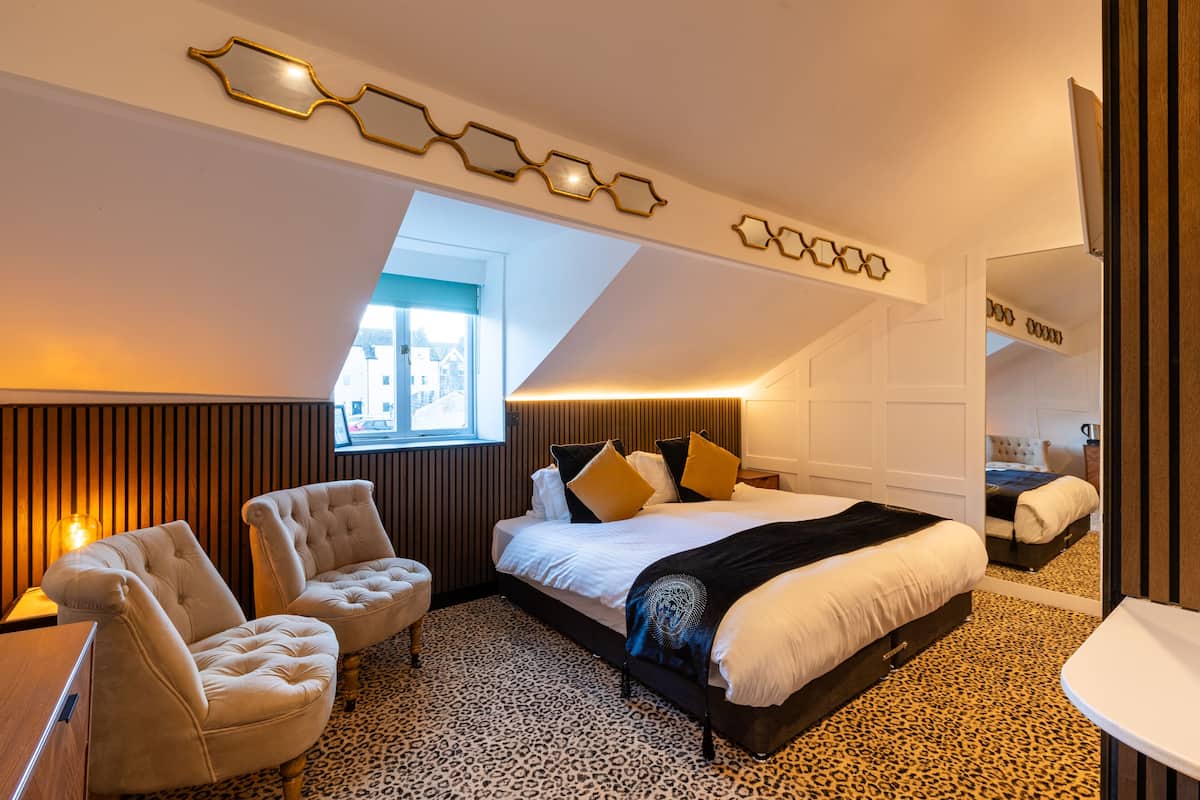 A modern bedroom with a large bed, two armchairs, a window, and a leopard print carpet.