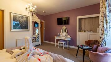 A hotel room with a bed, a vanity with a mirror, a television on the wall, and a floral curtain.