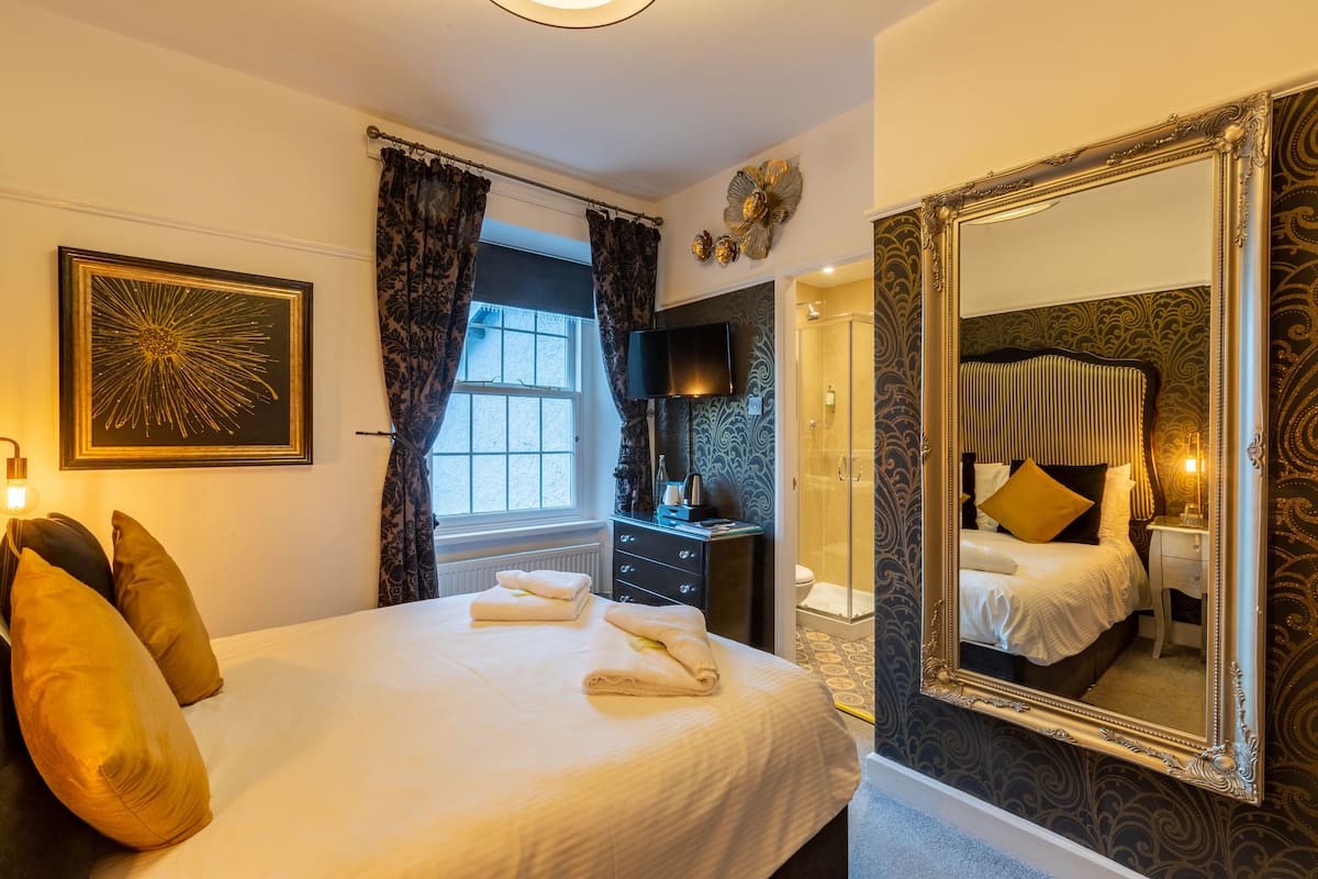 A well-lit bedroom with a large bed, a mirror, a dresser, and a window with curtains.