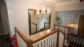 A staircase with a wooden railing, a chandelier, a fire extinguisher, a mirror, and a checkered floor.