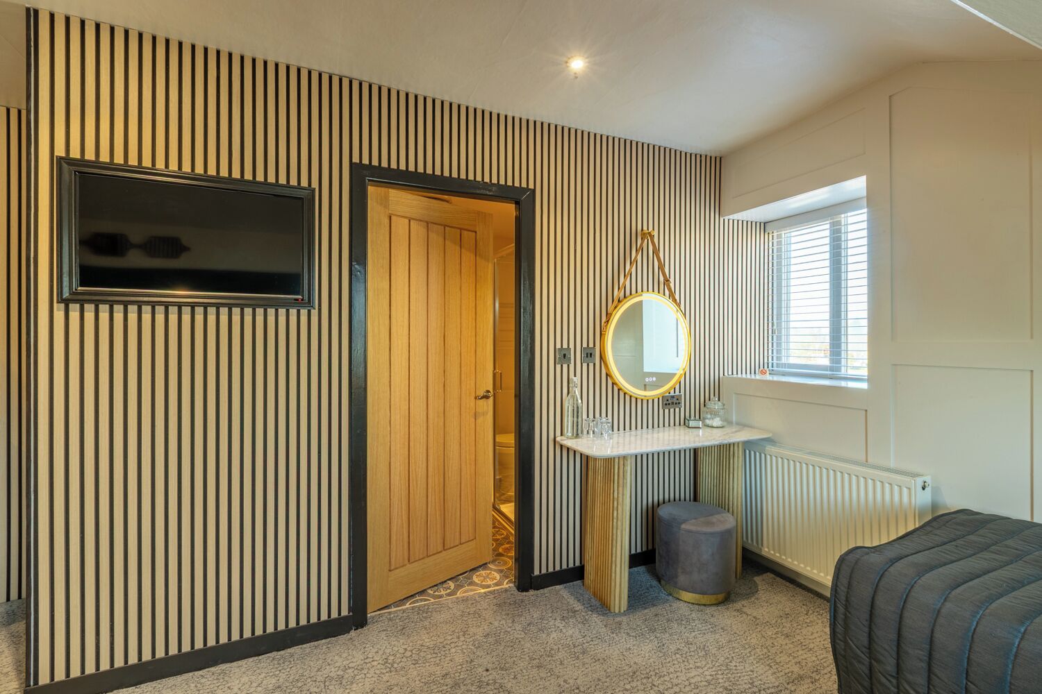 Una habitación con pared a rayas, puerta de madera, espejo, radiador y ventana.