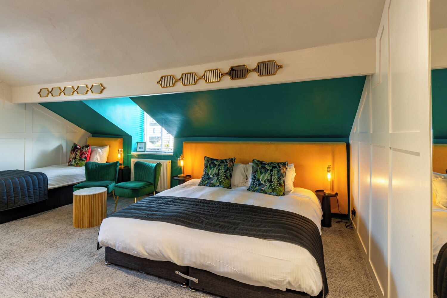 Habitación de hotel moderna con una cama grande, dos camas más pequeñas, sillas verdes y un diseño de techo único.