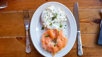A plate with a bagel topped with cream cheese and salmon, accompanied by a fork and knife on a wooden table.