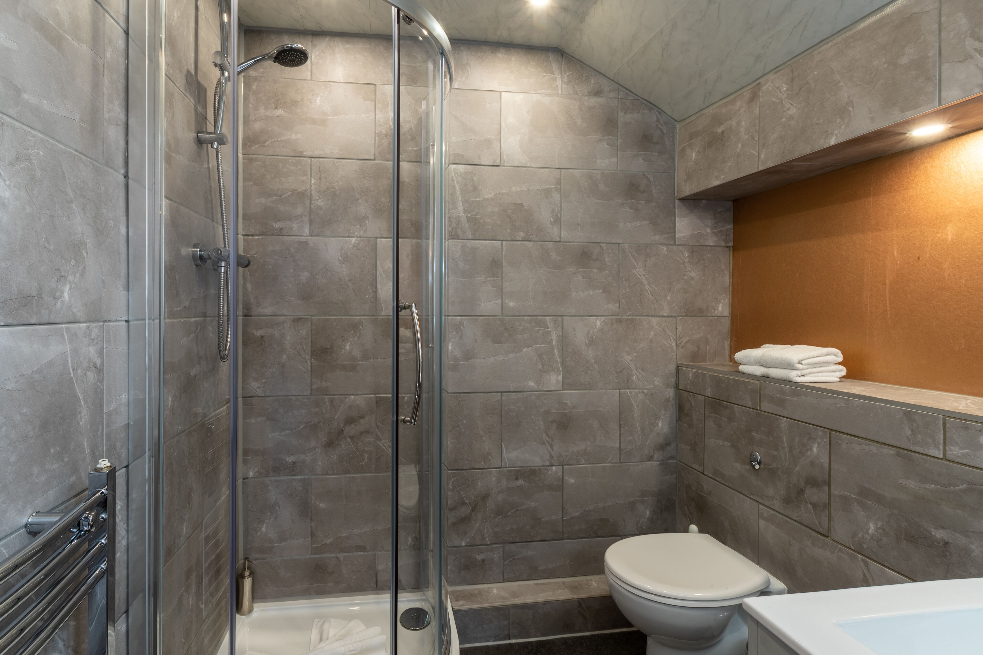 Un baño moderno con ducha envuelta en vidrio, inodoro y tocador con perchero para toallas.