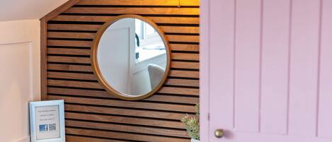 A reception area with a wooden slatted wall, a round mirror, a framed signboard, and a small potted plant.