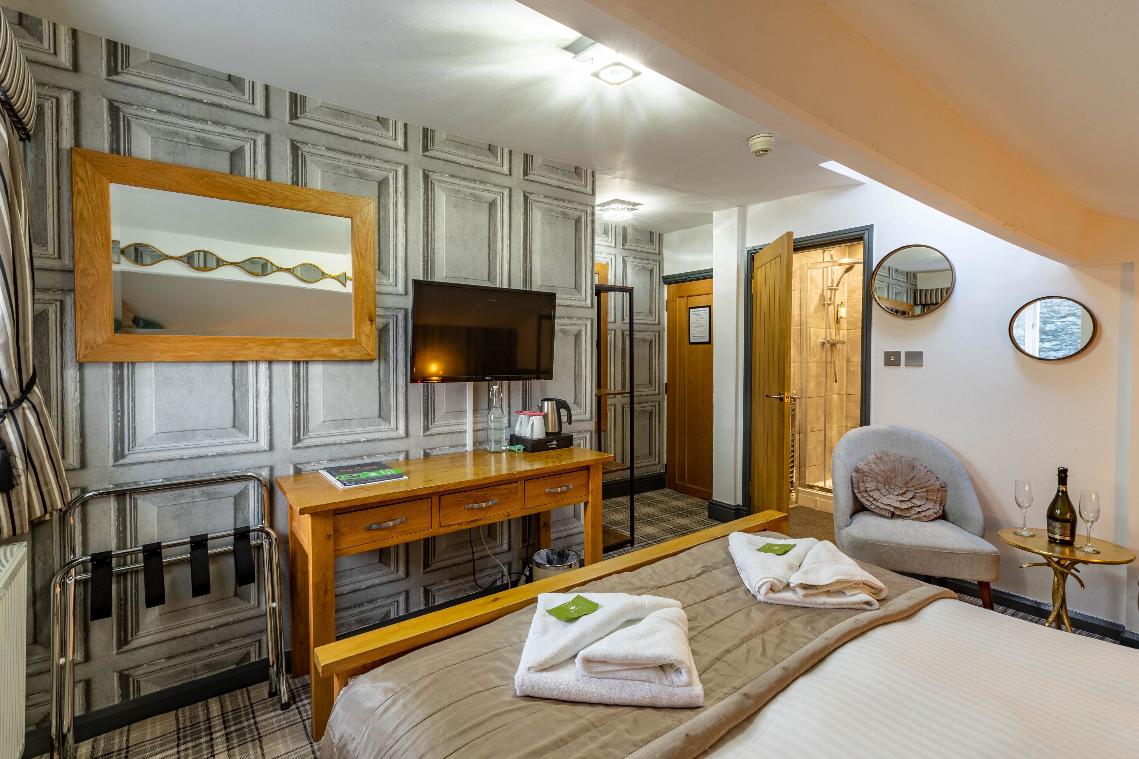 Una habitació d'hotel amb un llit gran, un escriptori de fusta, una televisió, un mirall i una cadira.