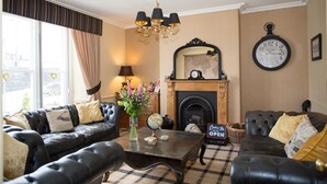 A living room with two black leather sofas, a wooden coffee table, a globe, and a fireplace. - Holly Lodge Guest House (Windermere)