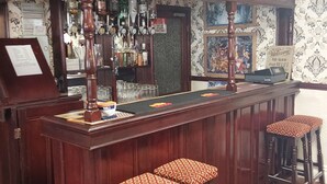 A bar area with a wooden counter, bar stools, and a variety of bottles. - Bianca Guesthouse (Blackpool)