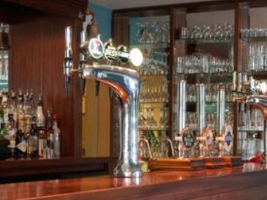 A bar area with a polished wooden counter, a large mirror, and shelves stocked with bottles and glasses.