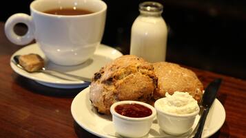 A plate with scones, butter, and jam, a cup of tea, and a salt shaker on a wooden table.